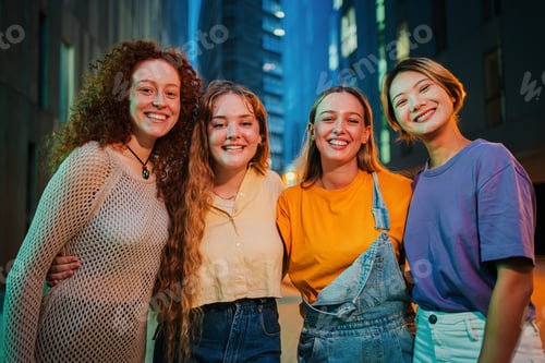 Preview: Portrait of a group of young women smiling looking at camera together at night time. Four female