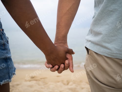 Preview: Detail of the holding hands of a multiethnic couple on the beach.