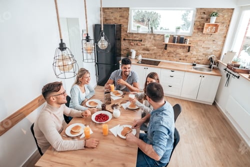 Preview: High angle image of five young people eating homemade pancakes in cozy apartment.