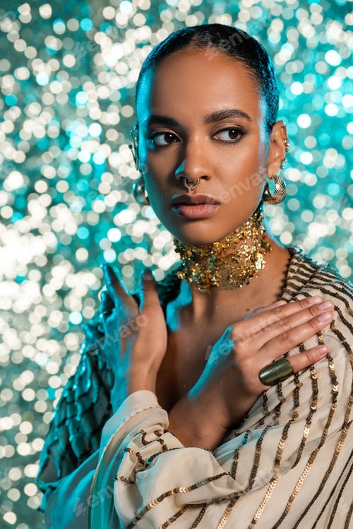Preview: pierced african american model with gold on neck posing with crossed arms on shiny blue background