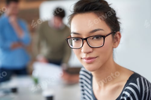Preview: Portrait of an attractive young woman sitting in an office with colleagues in the background