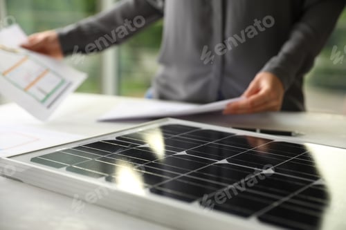 Preview: Solar panel and blurred person with papers on background, closeup