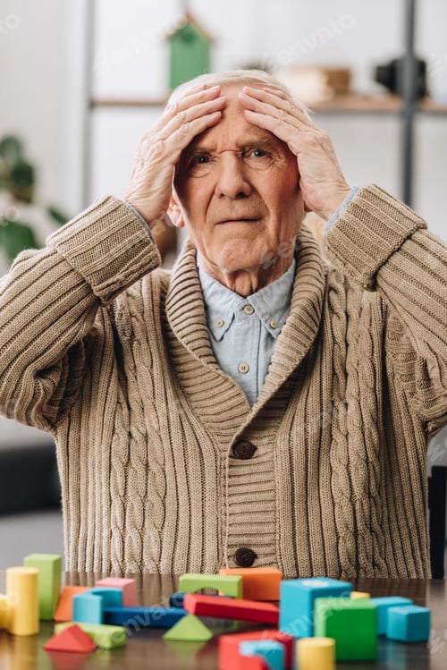 Preview: pensioner holding head while sitting near wooden toys at home