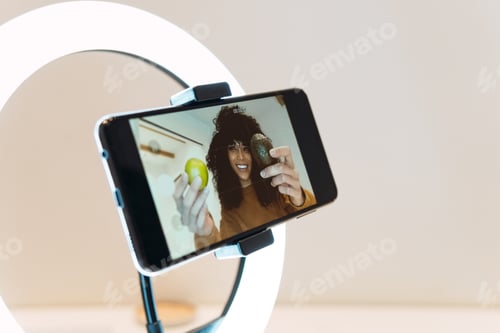 Preview: Phone on tripod filming video of female food blogger telling recipe in kitchen while recording vlog