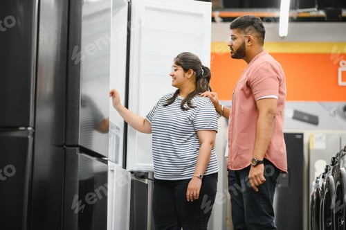 Preview: Young indian couple, satisfied customers choosing fridges in appliances store