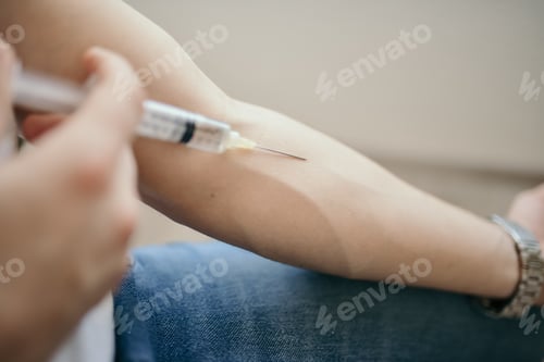 Preview: Selective focus shot of a person injecting medicine from a syringe at home