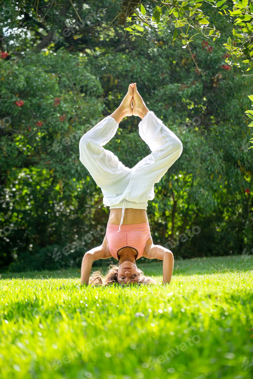Preview: Young Woman Standing on her Heads Doing Yoga in a Green Park.Vertical Image