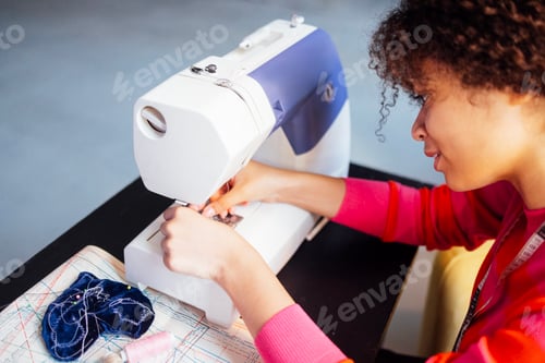 Preview: Young African woman working at sewing machine. Charming black girl in red sweater