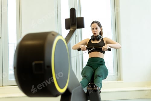 Preview: Focused woman engages in a rowing workout in a bright, modern gym during the morning hours