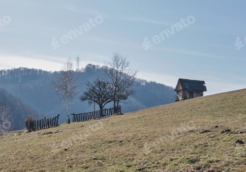 Preview: Low angle shot of a rural landscape with a small old house and wooden fence on the hill
