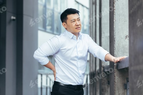 Preview: Tired asian businessman near office, doing back massage, has severe back pain, boss on break