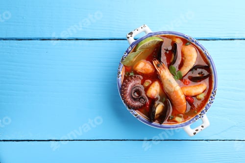 Preview: Delicious seafood soup in bowl on blue wooden table, top view. Space for text