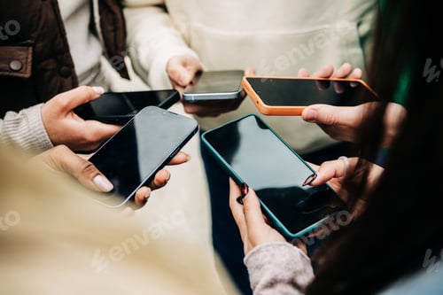 Preview: Young group of people using mobile phone together standing outdoor