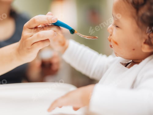 Preview: Mother at home feeding toddler baby jar food in high chair, childhood, parenthood
