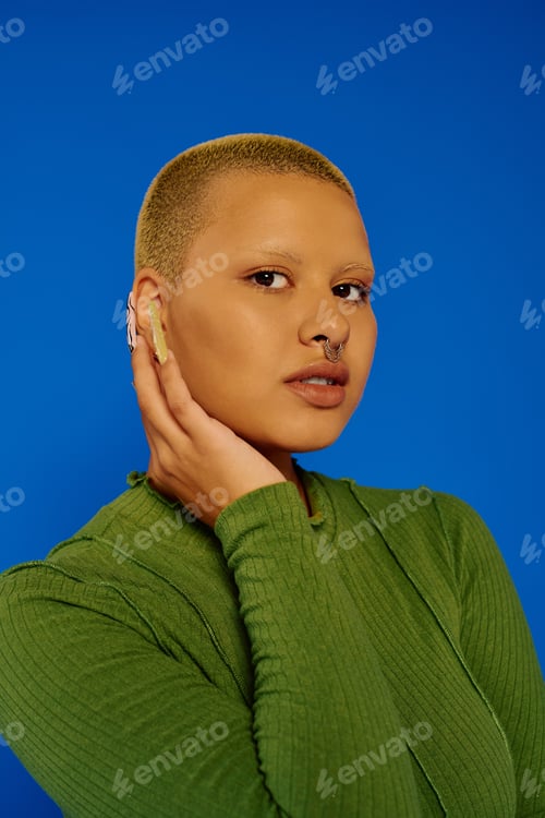 Preview: A young stylish woman poses confidently against a vibrant blue background in trendy attire