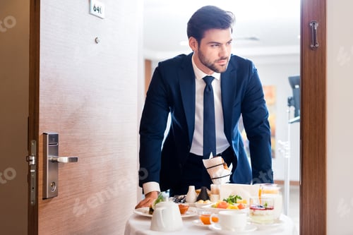 Preview: selective focus of handsome receptionist bringing breakfast on hotel food trolley