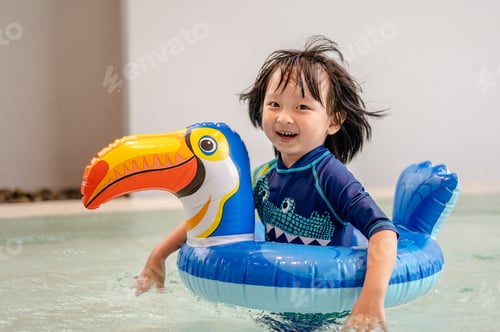 Preview: Portrait of little boy in swimming pool on funny inflatable hornbill float ring,learning how to swim