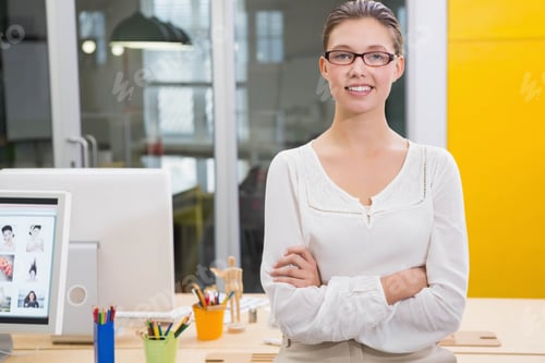 Preview: Woman in glasses and blouse standing at desk in office with monitor, pencils, mannequin, copy space