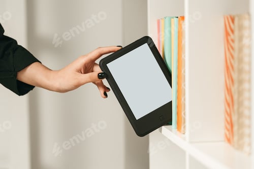 Preview: Man taking modern e-book reader from a bookshelf close up