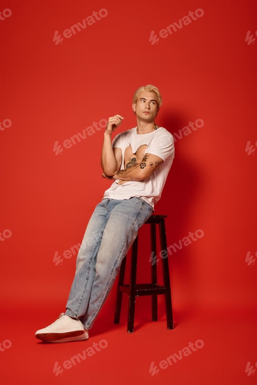 Preview: Stylish young man sitting on a stool against a vibrant red background