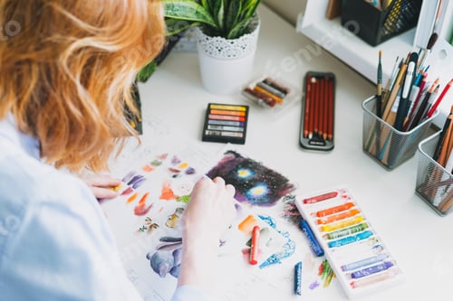 Preview: Young woman with red hair illustrator artist draws at desk at the home office