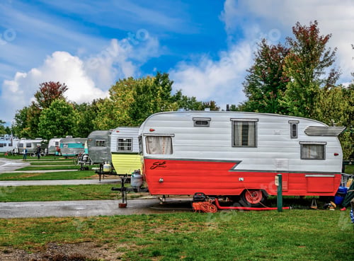 Preview: Colorful vintage trailers parked in a scenic campground with lush green trees and blue sky