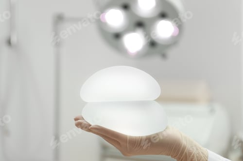 Preview: Doctor holding silicone implants for breast augmentation in clinic, space for text. Cosmetic surgery