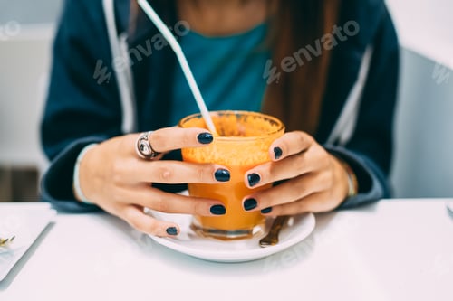Preview: Close up on the hands of a young woman holding a glass of juice - health, break, relaxing concept
