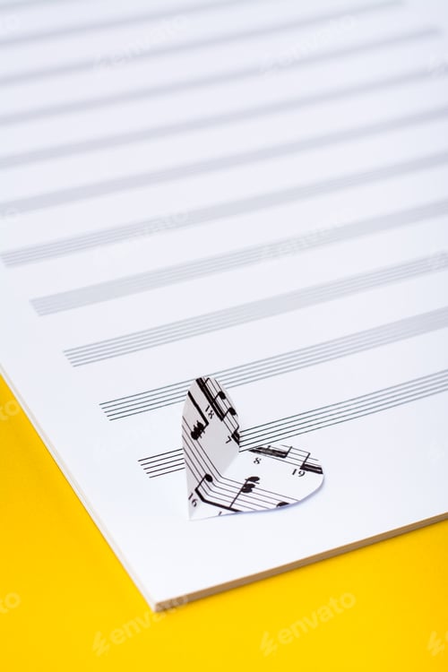 Preview: Blank sheet music and hearts cut from music text on yellow background. Vertical view