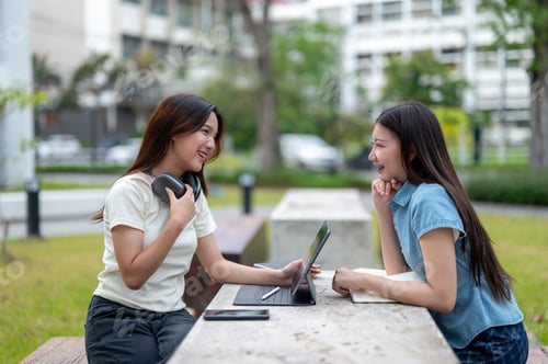 Preview: Two women sitting at a table, one of them is using a laptop