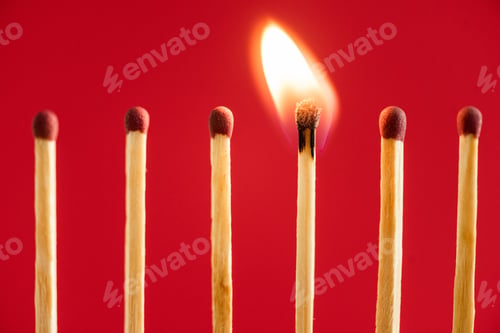 Preview: Match with fire among burned matches on red