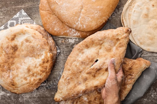 Preview: cropped view of man holding lavash bread on brown wooden table