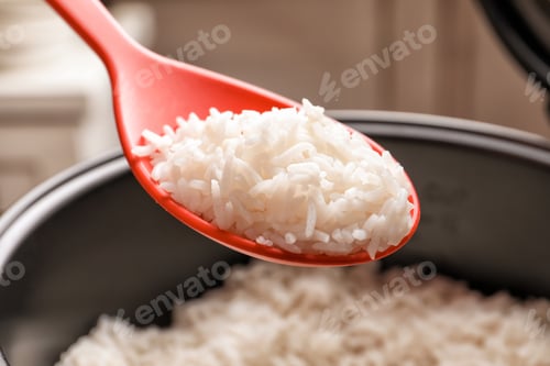 Preview: Spoon with tasty hot rice over cooker, closeup