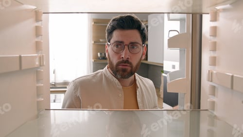 Preview: Hungry Caucasian bachelor man looking for food in empty fridge finding no meal products feeling sad