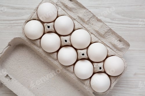 Preview: Uncooked Organic White Eggs in a paper box on a white wooden background, top view.