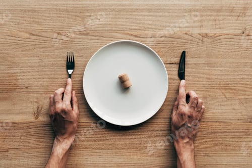 Preview: cropped view of man holding fork and knife at table with plate and cork