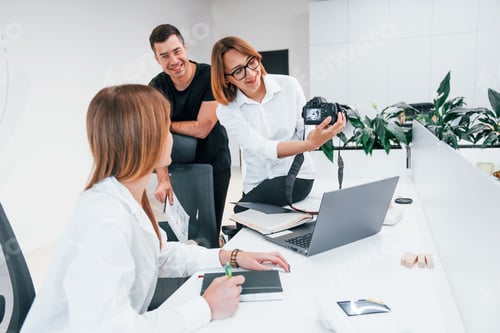 Preview: Group of business people in formal clothes indoors in the office looking at photos on the camera
