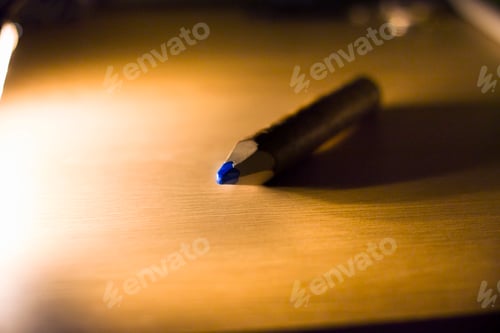 Preview: Top view of blue sharp pencil lying on wooden yellow table or desk surface