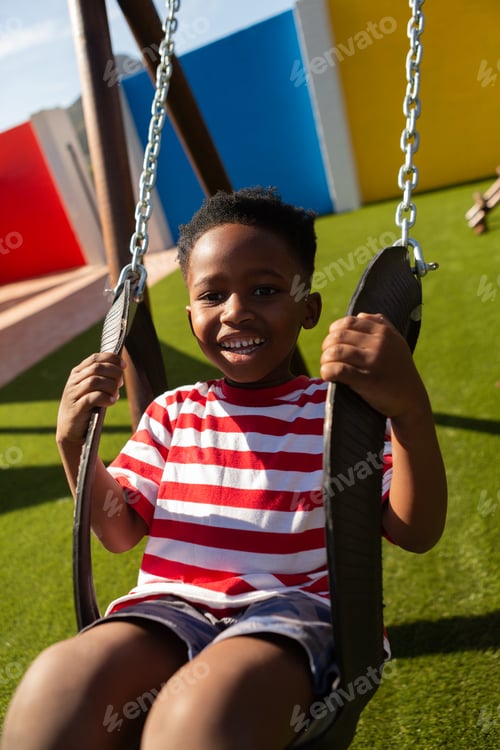 Preview: Happy schoolboy playing on a swing at school playground on a sunny day