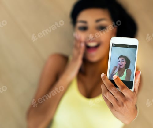 Preview: OMG. Shot of a young woman taking a selfie while lying on a wooden floor.