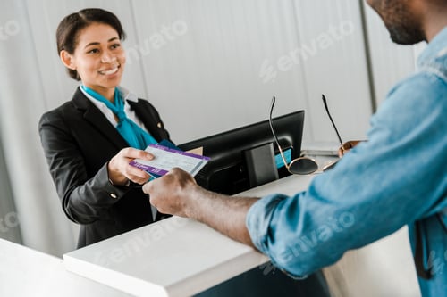 Preview: cheerful african american airport worker giving passport and air ticket to tourist
