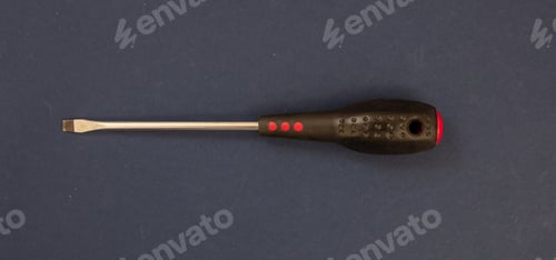 Preview: Slot head screwdriver red black rubber handle on blue background. Overhead close up view. Banner