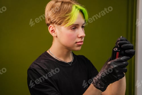 Preview: Young man tattoo artist with colored hair and piercing preparing for work indoor. Small business