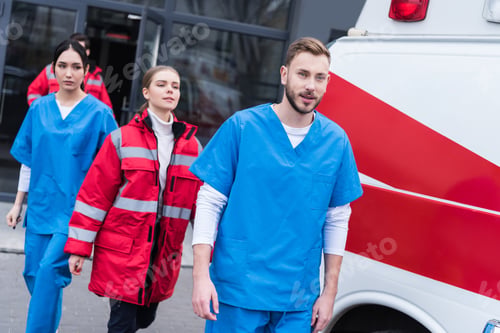 Preview: young male and female paramedics walking near ambulance