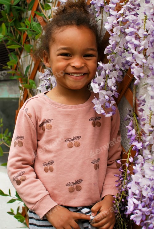Preview: Portrait of a toddler girl in front of purple wisteria flowers - petals pink mixed race diversity