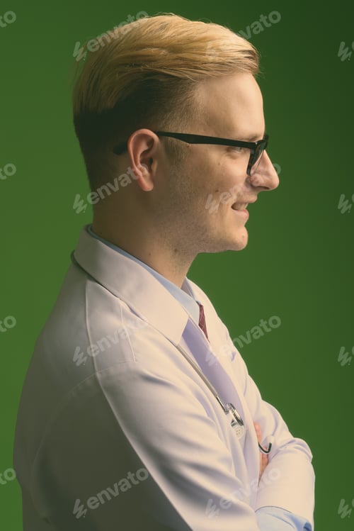 Preview: Young handsome man doctor with blond hair against green background