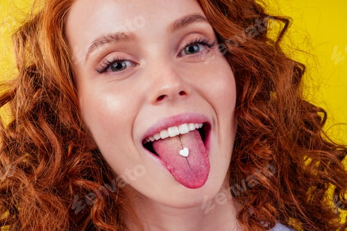 Preview: redhaired ginger afro curly woman taking happy love pills in studio .heart shape pill