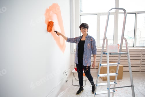 Preview: Happy middle-aged woman painting wall in her new apartment. Renovation, redecoration and repair