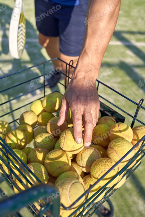 Preview: Crop man taking tennis ball from basket on playground