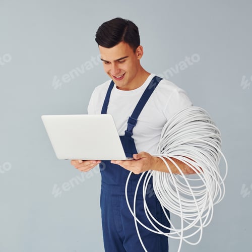 Preview: Uses laptop. Male worker in blue uniform standing inside of studio against white background